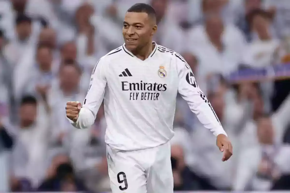 Un jugador de fútbol con uniforme blanco celebrando en un estadio lleno de espectadores.