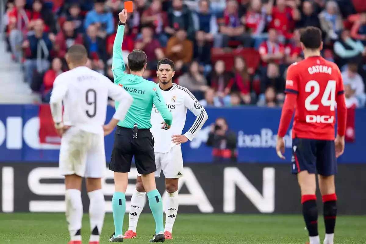 Un árbitro muestra una tarjeta roja a un jugador de fútbol en un partido mientras otros jugadores observan.