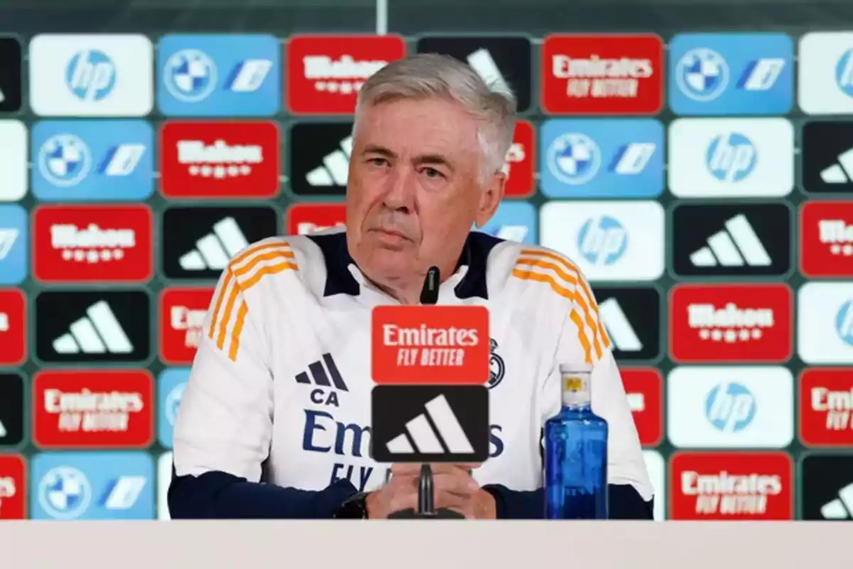 A man at a press conference with a background of sports sponsor logos.