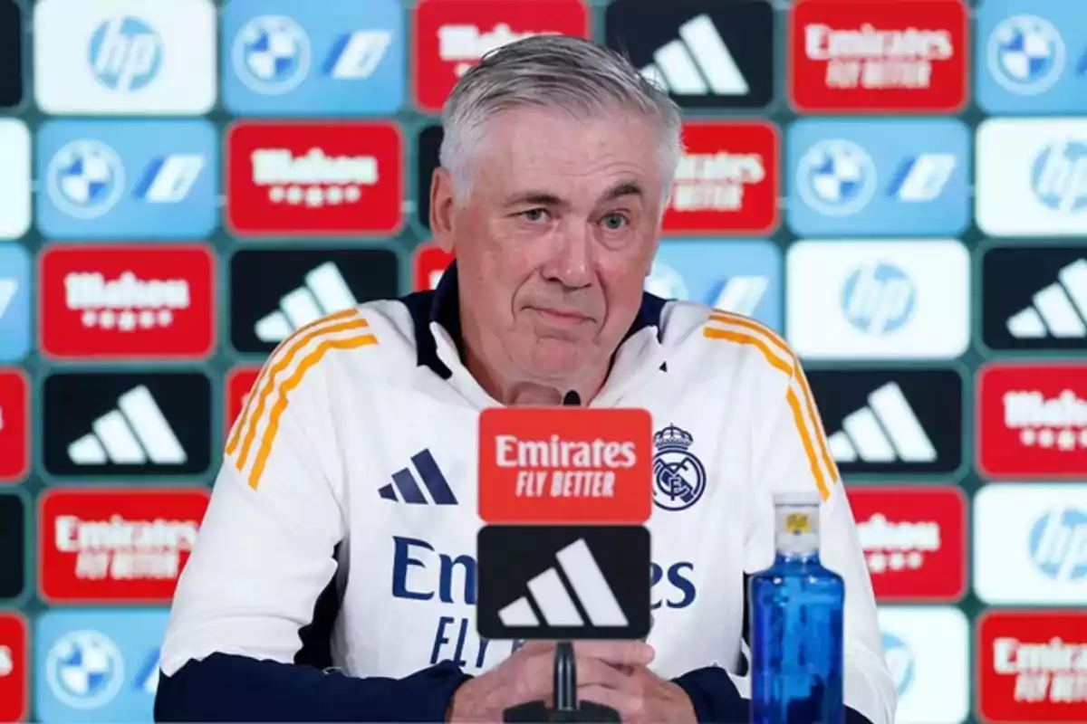 A man at a press conference with a backdrop of sponsor logos.