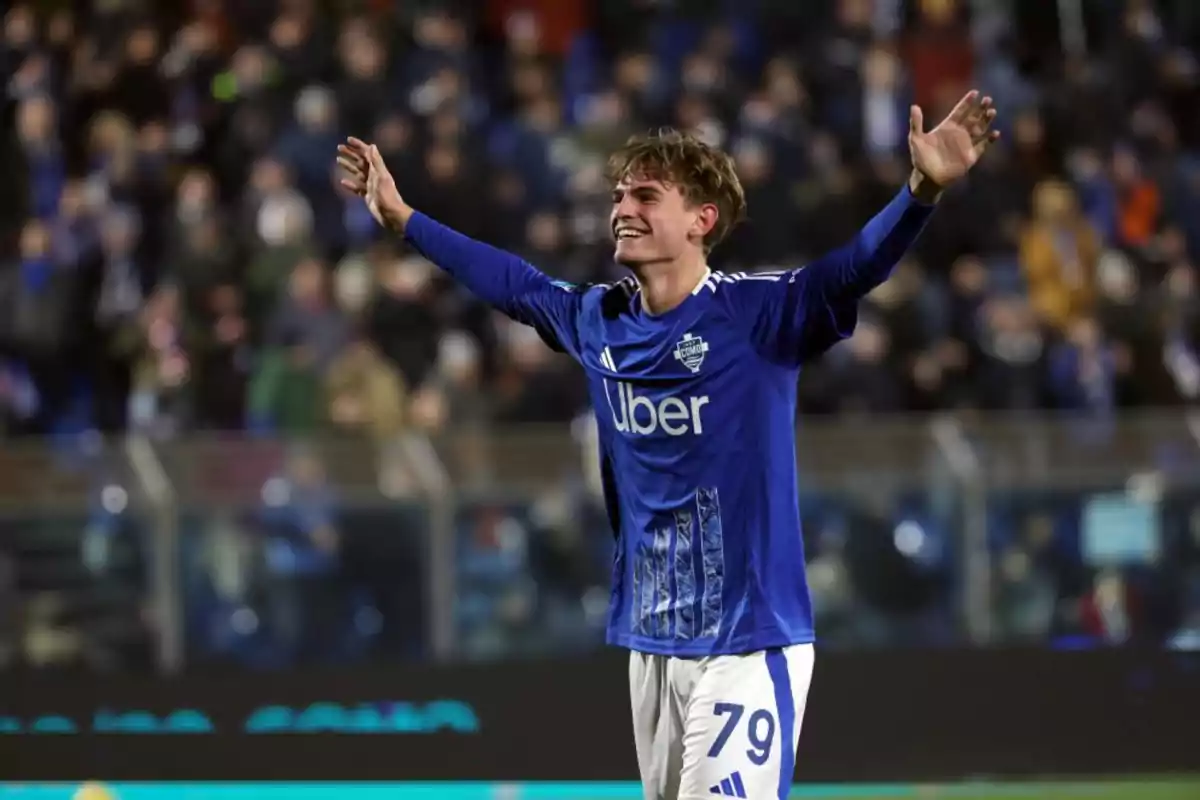 A player in a blue uniform celebrates with open arms in a stadium full of spectators. A player in a blue uniform celebrates with open arms in a stadium full of spectators.