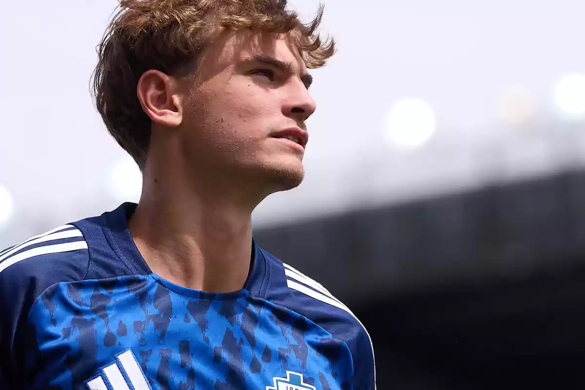 A young man in a blue and white sports jersey looks toward the horizon in an outdoor setting. A young man in a blue and white sports jersey looks toward the horizon in an outdoor setting.