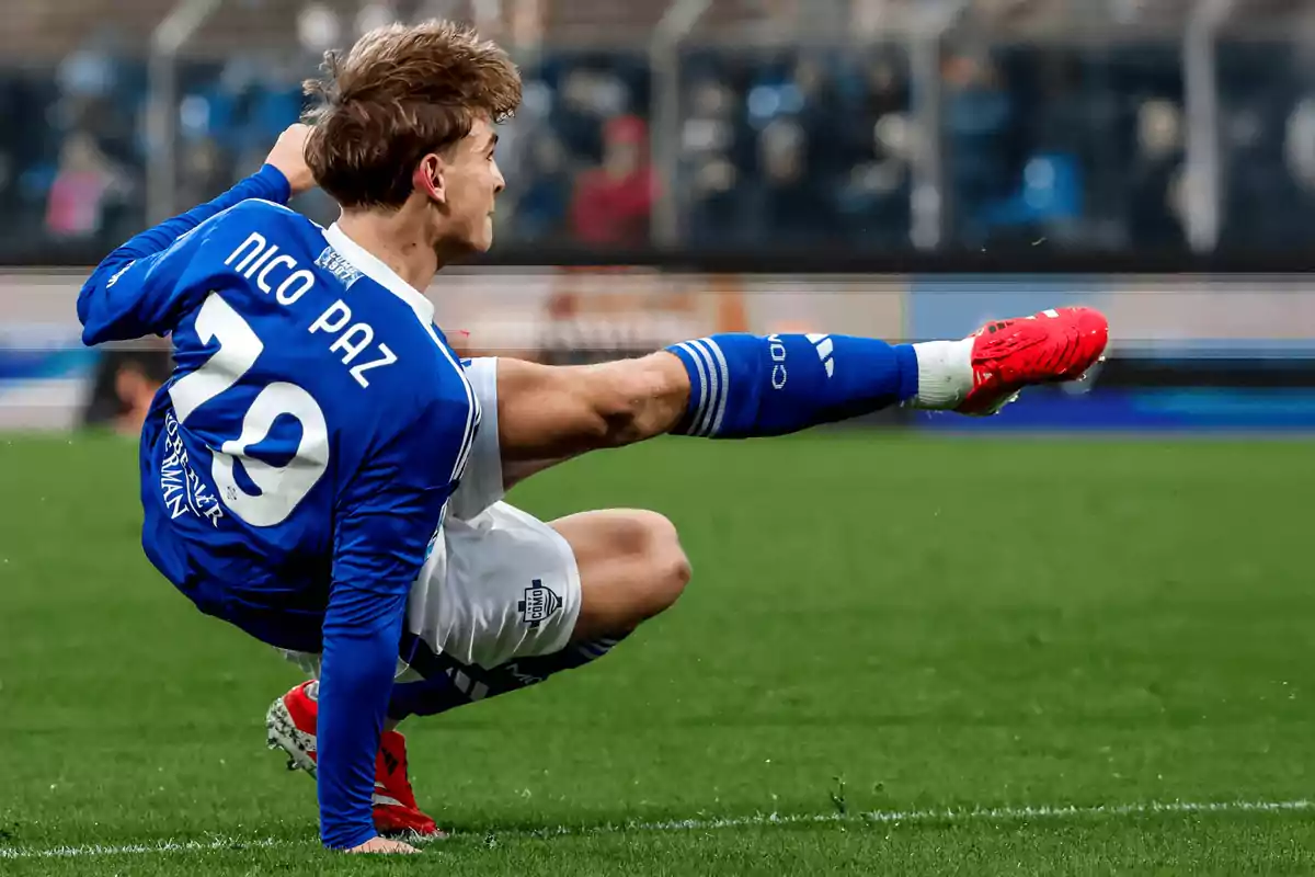 Jugador de fútbol con uniforme azul y blanco realizando una acrobacia en el campo durante un partido Jugador de fútbol con uniforme azul y blanco realizando una acrobacia en el campo durante un partido