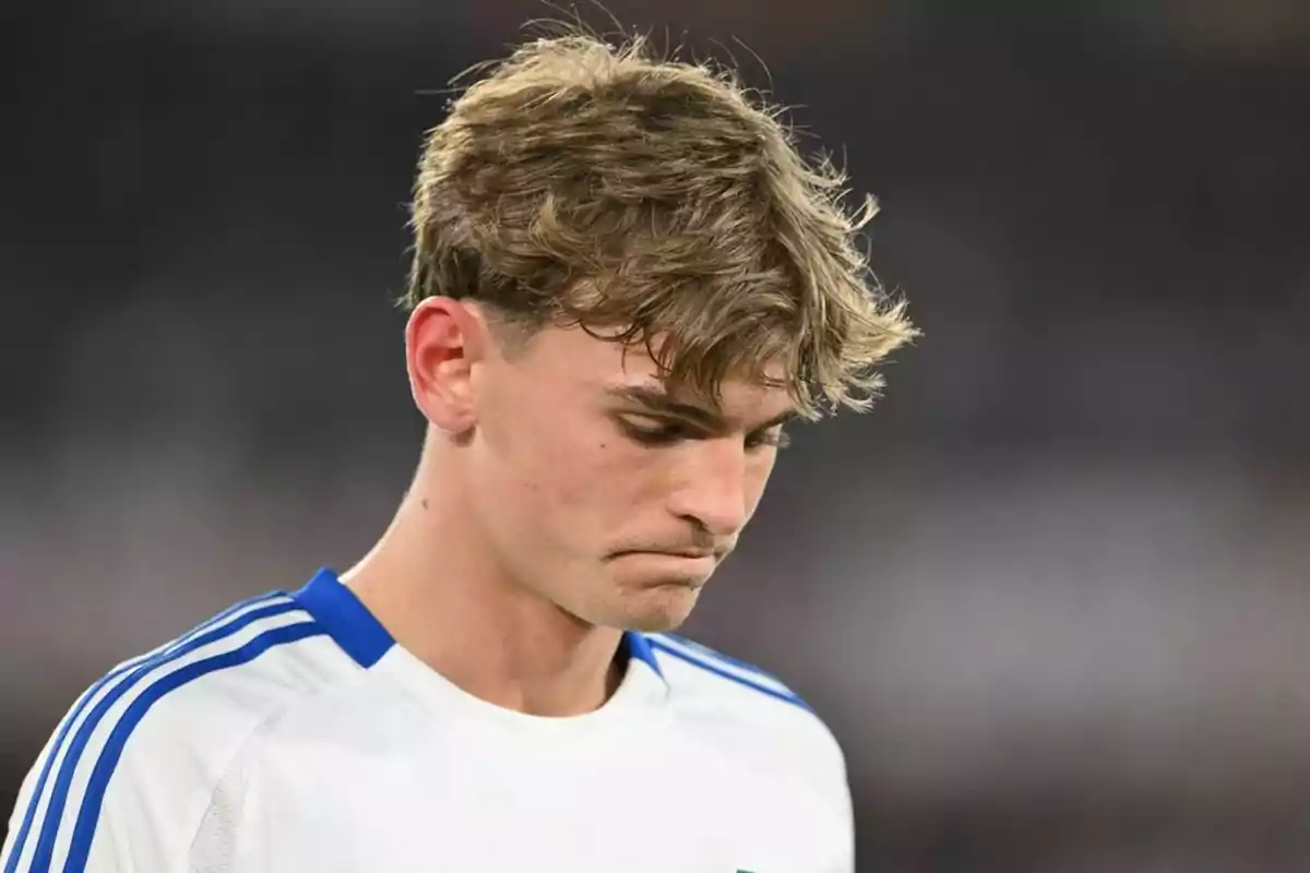 A young man in a white and blue sports jersey looks down with a thoughtful expression. A young man in a white and blue sports jersey looks down with a thoughtful expression.