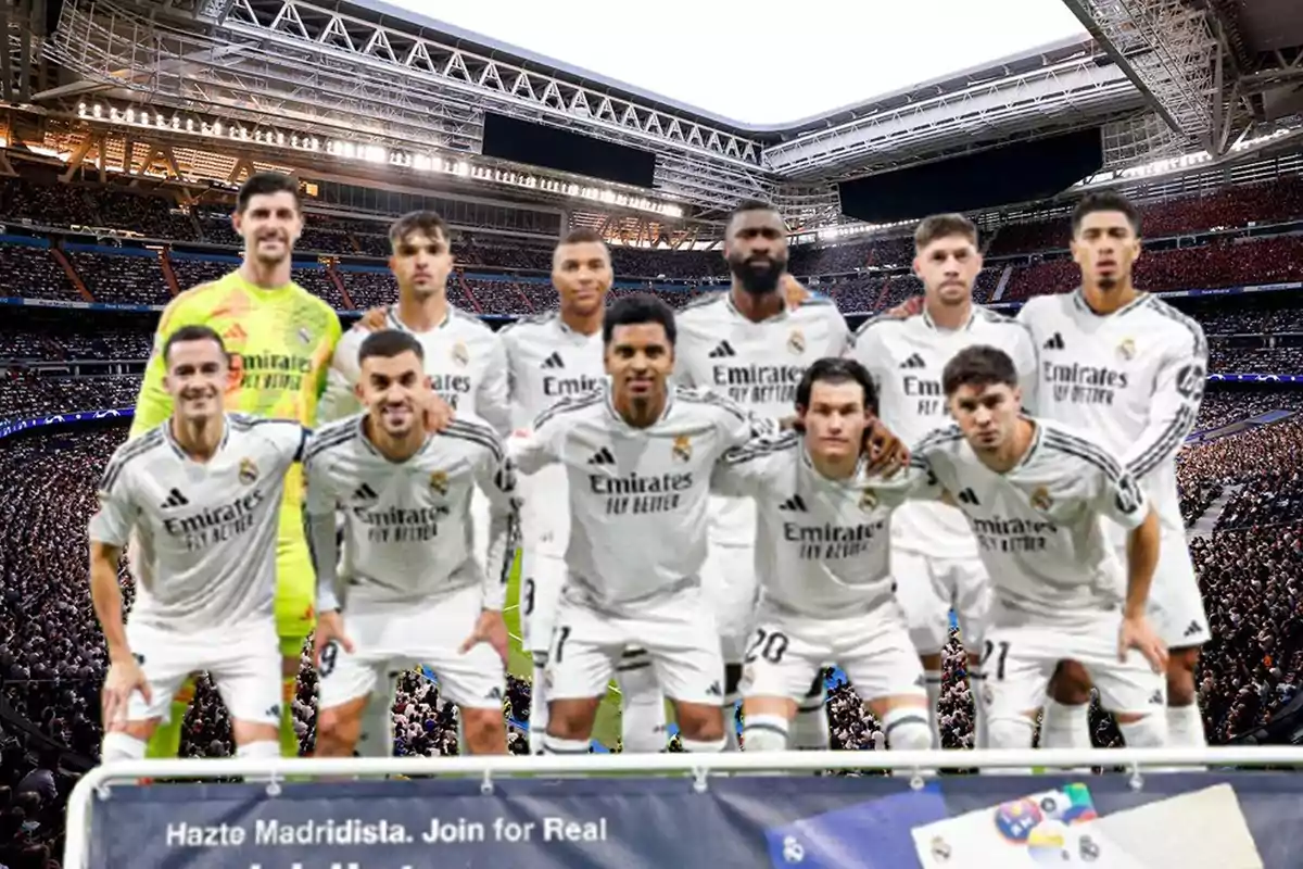 A soccer team posing on the field of a stadium full of spectators.