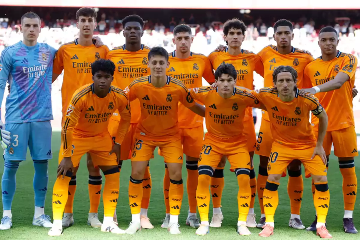 Real Madrid players posing on the field in orange uniforms before a match.