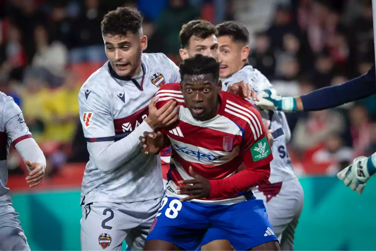 Players from two soccer teams compete for position during a match, one wearing a red and white uniform and the other wearing a gray uniform. Players from two soccer teams compete for position during a match, one wearing a red and white uniform and the other wearing a gray uniform.