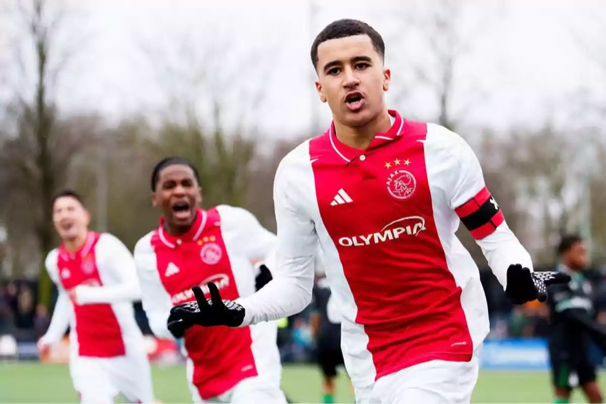 Ajax player celebrating a goal in a soccer match with teammates in the background showing excitement Ajax player celebrating a goal in a soccer match with teammates in the background showing excitement
