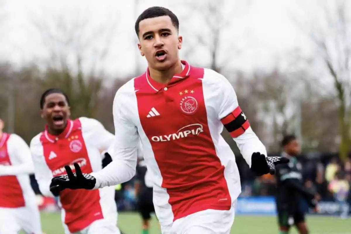 Young Ajax footballer celebrating a goal on the field with teammates in the background Young Ajax footballer celebrating a goal on the field with teammates in the background