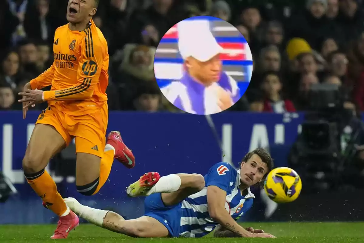 Un jugador de fútbol con uniforme naranja parece estar cayendo al suelo mientras otro jugador con uniforme azul y blanco está en el suelo mirando hacia él; en la parte superior de la imagen hay un círculo que muestra un acercamiento de una persona con gorra blanca.