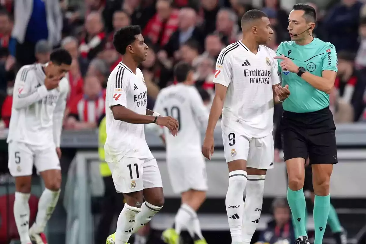 Real Madrid soccer players on the field during a match, one of them interacting with the referee.