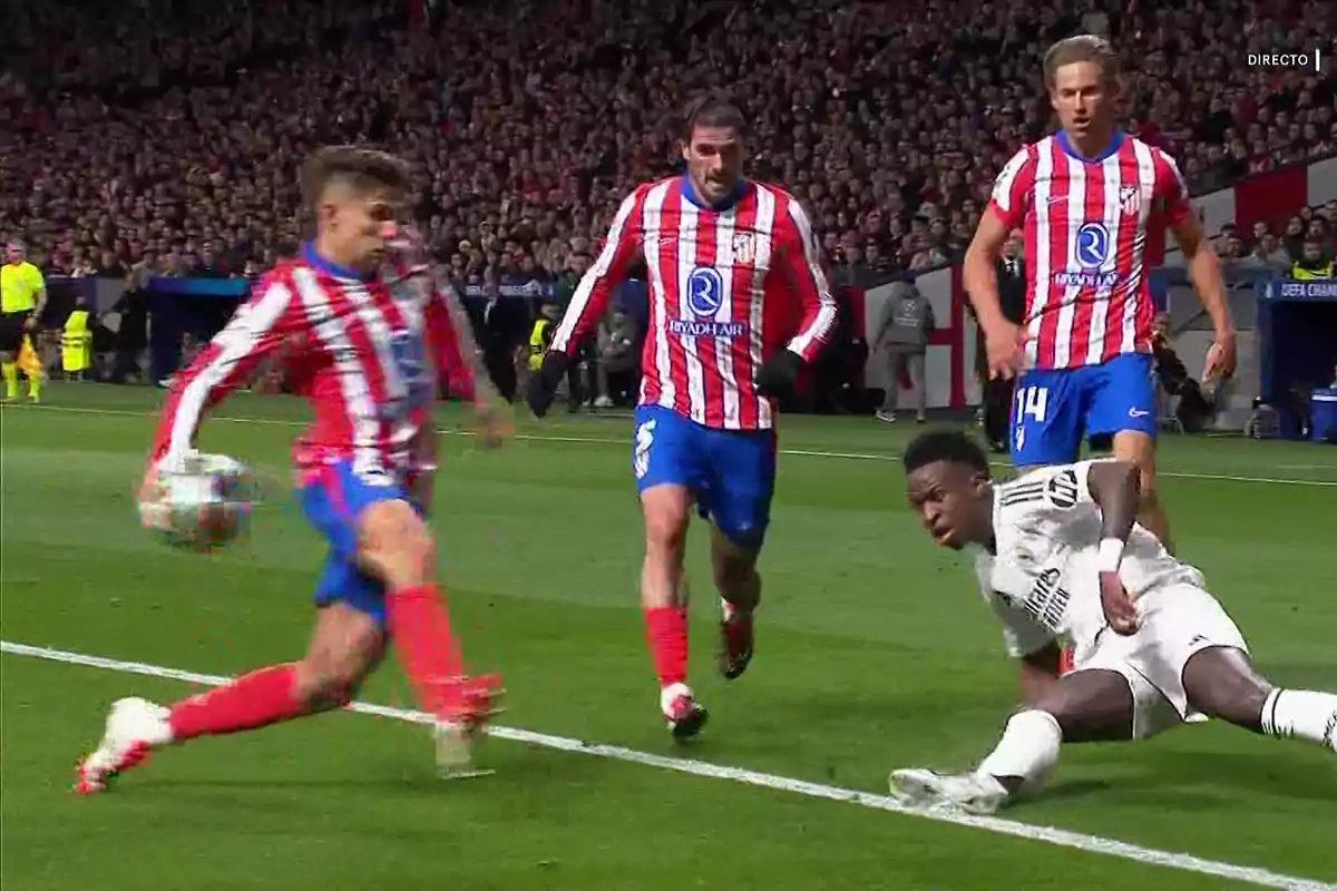 Soccer players in action during a match, one of them falls to the ground while three others in red and white striped uniforms approach.