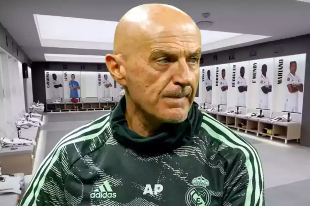 A bald man in a Real Madrid training uniform is in a team locker room with jerseys and photos of players in the background.