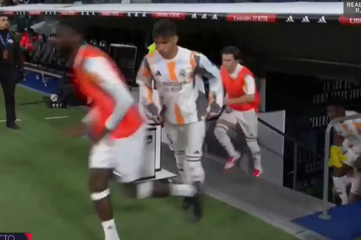 Jugadores de fútbol con petos naranjas salen corriendo desde el túnel hacia el campo de juego.