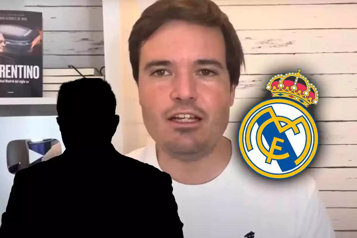 Un hombre frente a una pared de madera clara con el escudo del Real Madrid a su lado y un libro en un estante detrás.