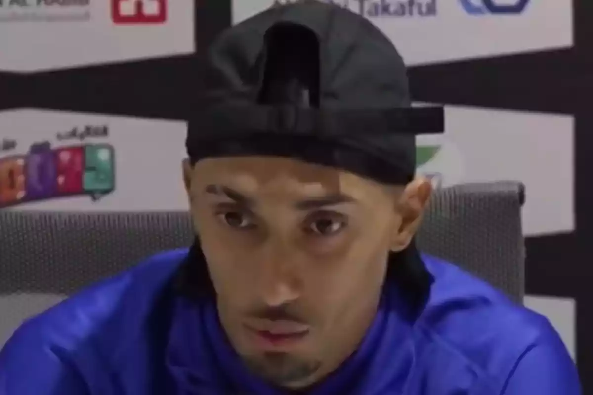A man wearing a backwards black cap and blue t-jersey at a press conference. A man wearing a backwards black cap and blue t-jersey at a press conference.