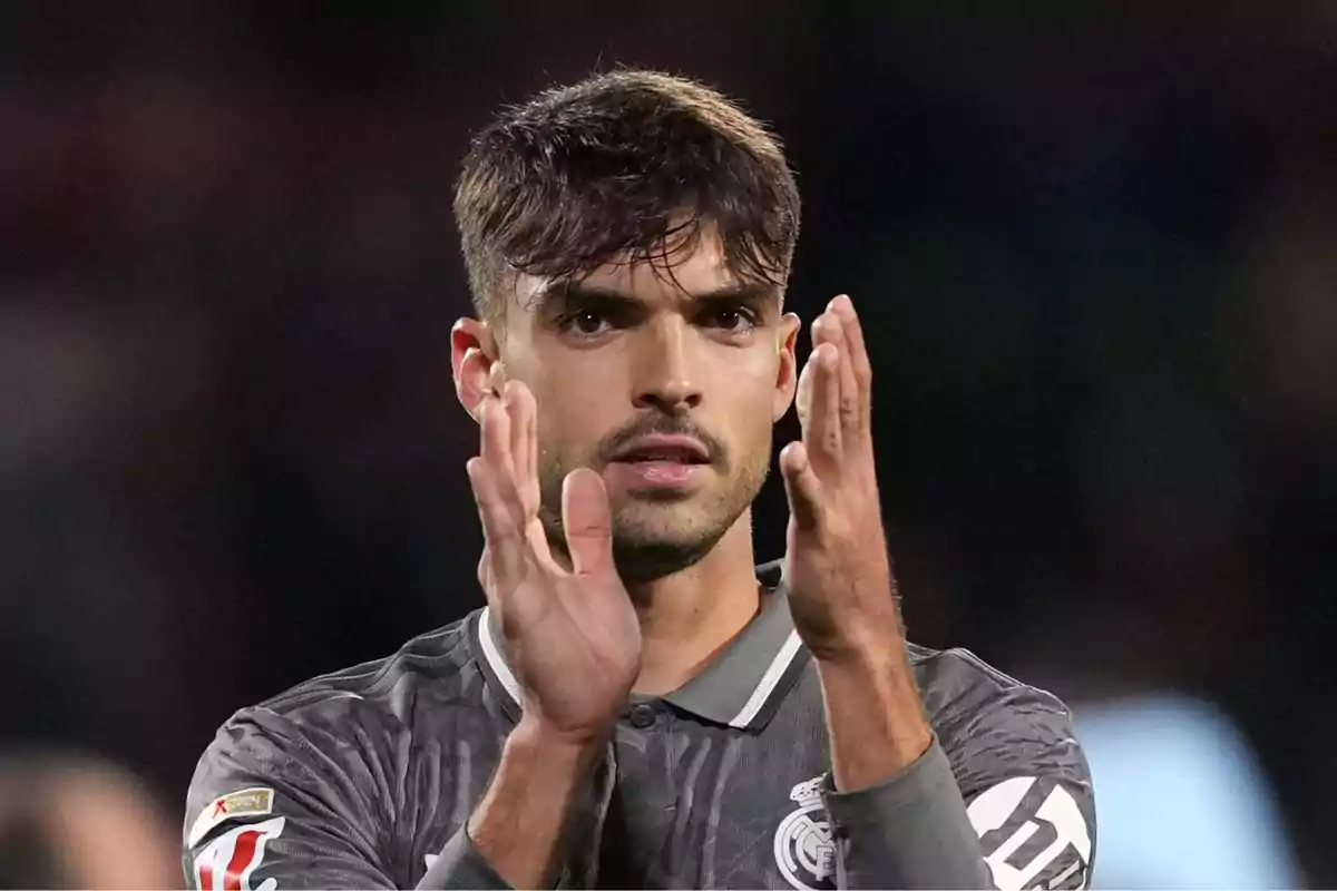 Un jugador de fútbol aplaudiendo en el campo con una camiseta gris.