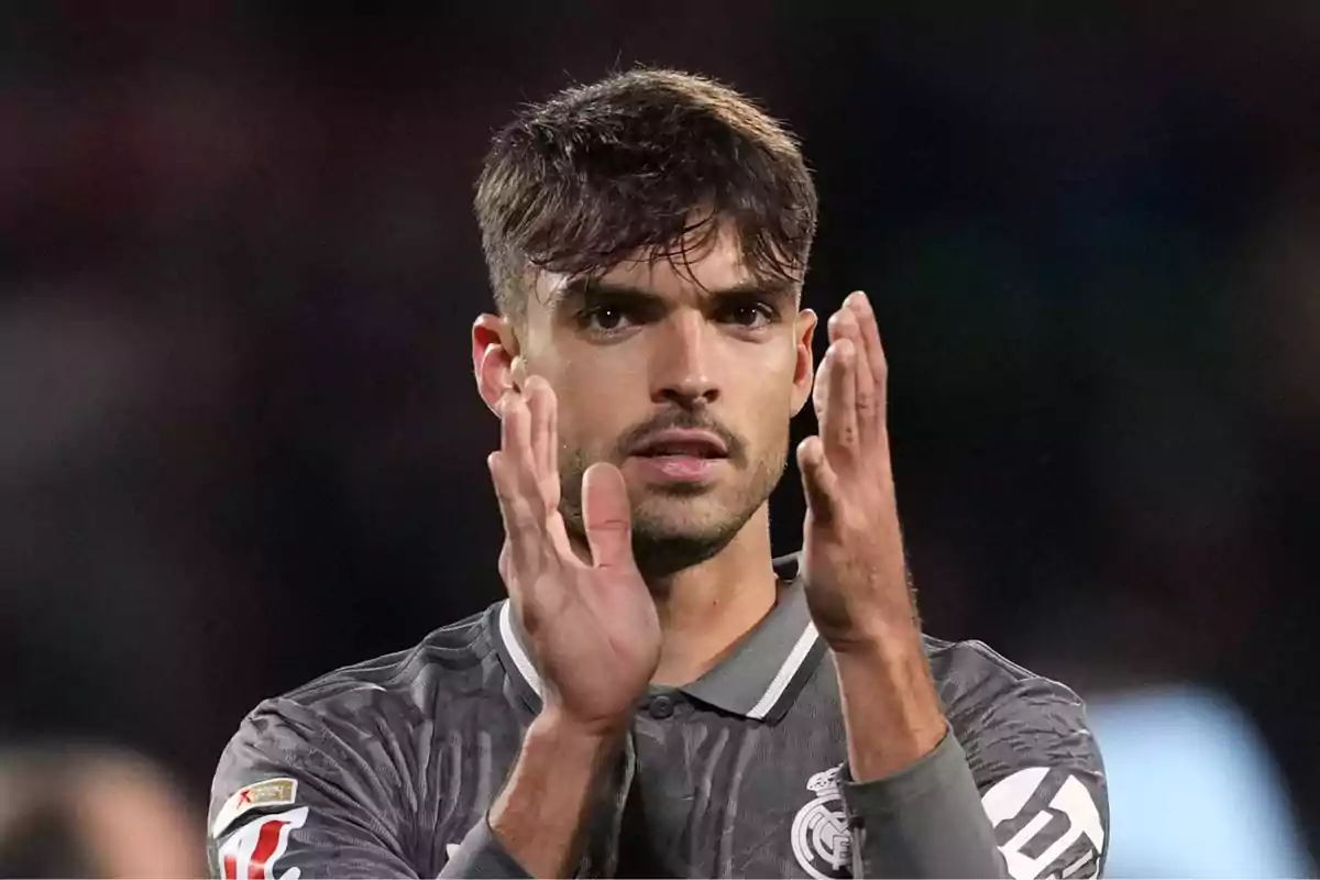 A soccer player applauding on the field in a grey uniform.