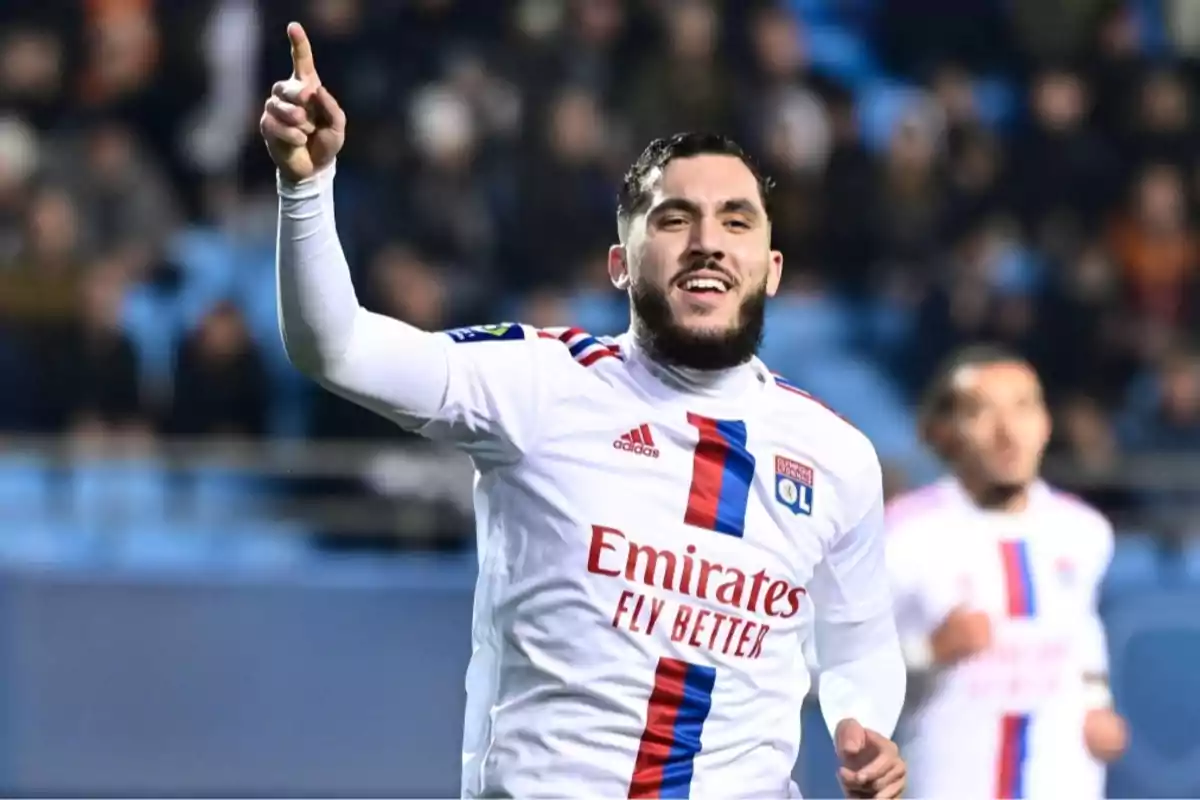 Un jugador de fútbol con uniforme blanco celebra levantando un dedo en un estadio lleno de espectadores. Un jugador de fútbol con uniforme blanco celebra levantando un dedo en un estadio lleno de espectadores.