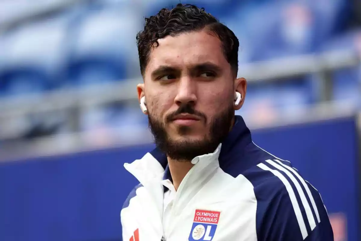 Un hombre con auriculares y chaqueta deportiva del Olympique Lyonnais en un estadio. Un hombre con auriculares y chaqueta deportiva del Olympique Lyonnais en un estadio.