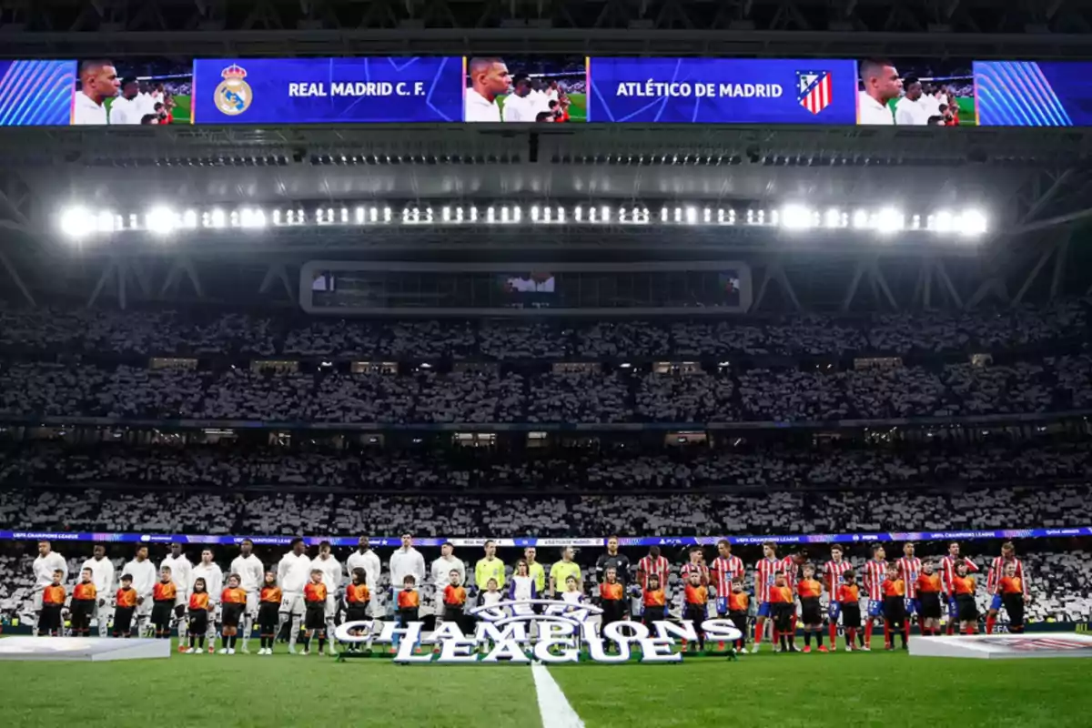 Players from two soccer teams lined up on the field before a Champions League match, with a stadium full of spectators and screens displaying the teams' names.