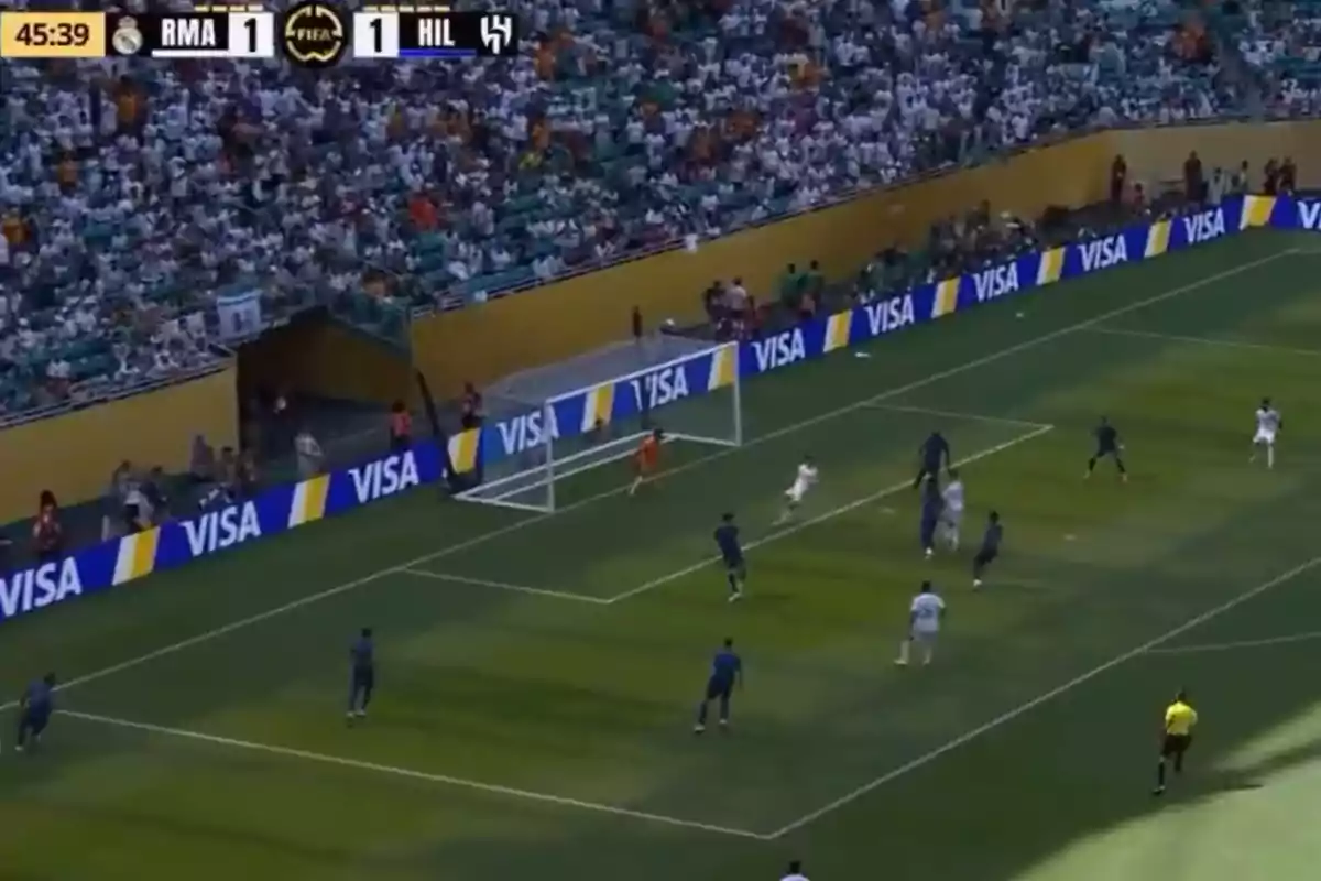 Partido de fútbol con jugadores en el área y el marcador empatado a uno entre Real Madrid y Al Hilal, con la tribuna llena de aficionados.