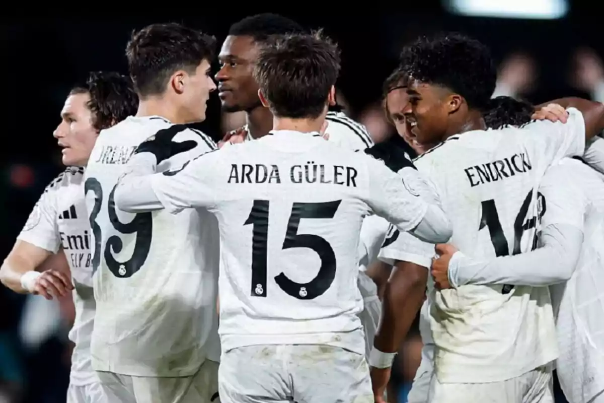 A group of soccer players in white uniforms hug each other on the field.