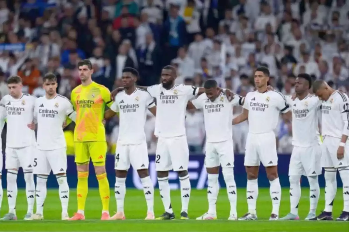 Soccer players in a row with white uniforms and a goalkeeper with a yellow uniform in a stadium full of spectators.