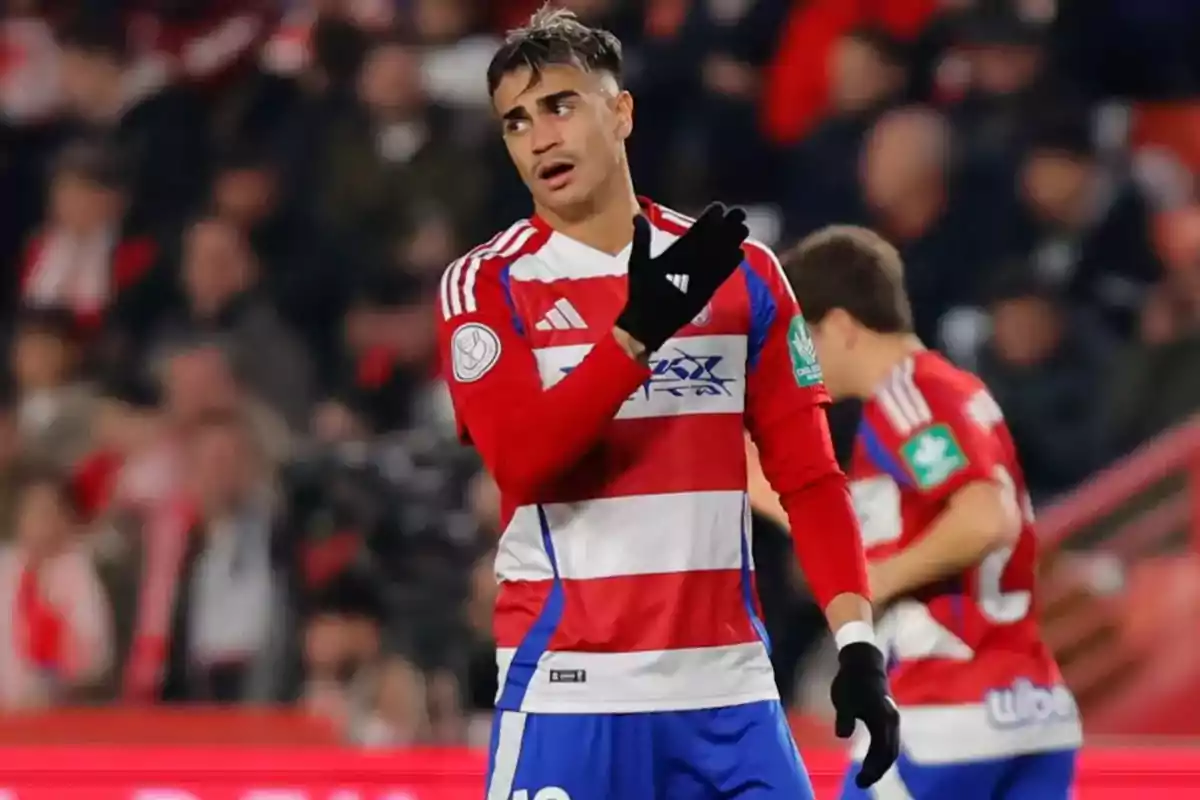 Futbolista con uniforme rojo y blanco en el campo durante un partido señalando con la mano enguantada y expresión seria Futbolista con uniforme rojo y blanco en el campo durante un partido señalando con la mano enguantada y expresión seria
