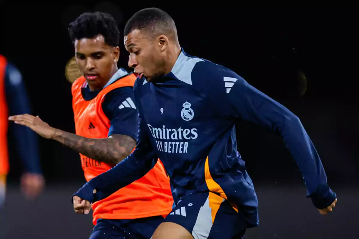 Two players training on a soccer field, one wearing an orange bib and the other wearing a dark blue uniform. Two players training on a soccer field, one wearing an orange bib and the other wearing a dark blue uniform.