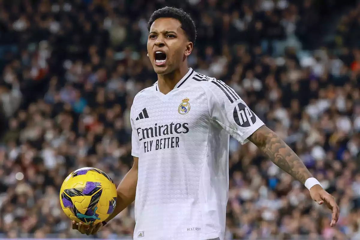 Un jugador de fútbol con uniforme blanco sostiene un balón amarillo en un estadio lleno de espectadores. Un jugador de fútbol con uniforme blanco sostiene un balón amarillo en un estadio lleno de espectadores.
