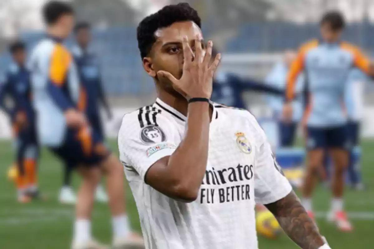 A football player wearing a Real Madrid jersey partially covers his face with his hand at a training ground.