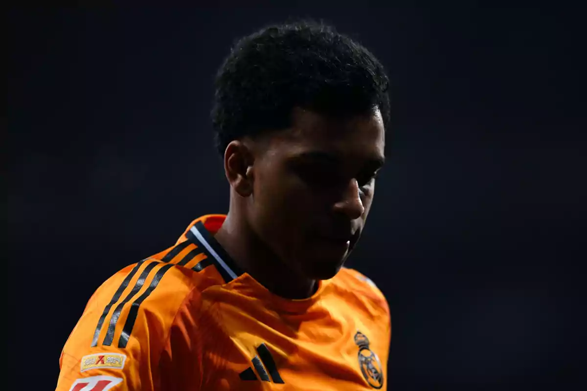 Un jugador de fútbol con uniforme naranja del Real Madrid en un entorno oscuro. Un jugador de fútbol con uniforme naranja del Real Madrid en un entorno oscuro.