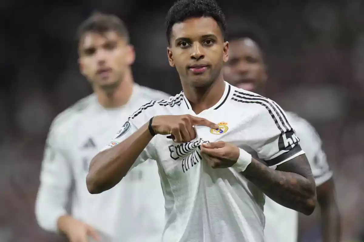 Un jugador de fútbol con uniforme blanco señala el escudo de su camiseta durante un partido. Un jugador de fútbol con uniforme blanco señala el escudo de su camiseta durante un partido.
