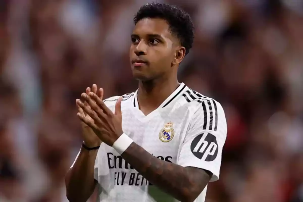 Soccer player in a white uniform clapping in a stadium.