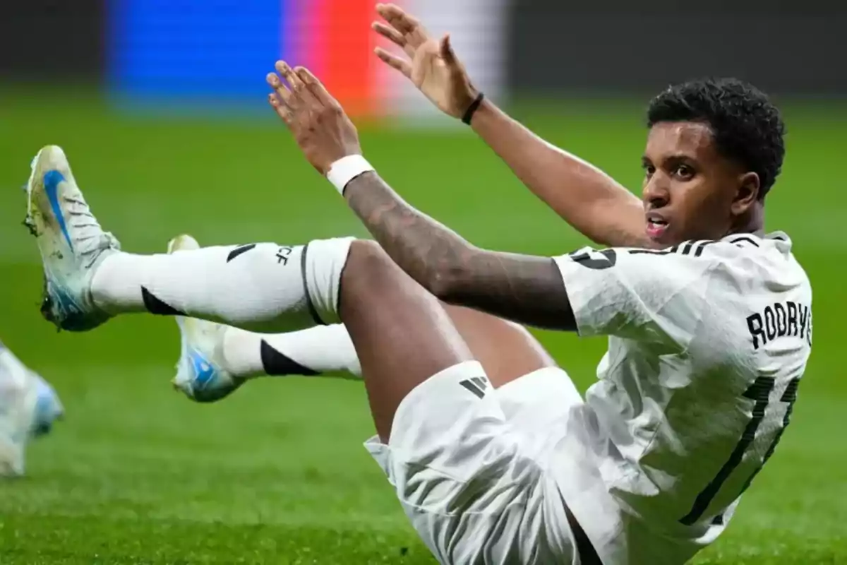 Jugador de fútbol con uniforme blanco sentado en el campo durante un partido.