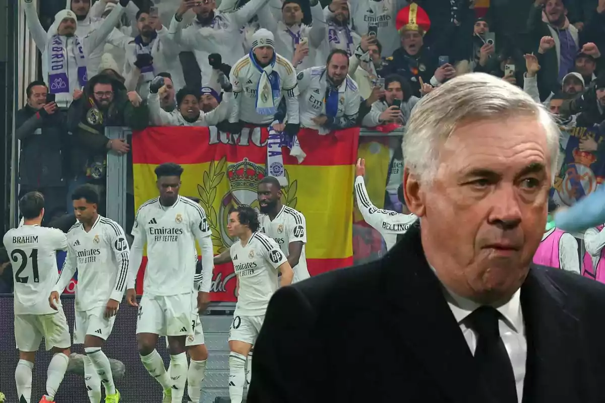 A group of soccer players in white uniforms celebrate in front of a crowd of fans holding a Spanish flag, while a man in a dark suit appears in the foreground.