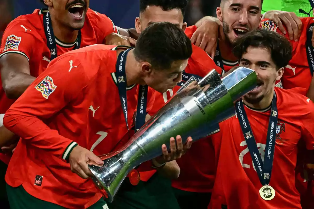Soccer players celebrate with a trophy, wearing red uniforms and medals after winning a tournament. Soccer players celebrate with a trophy, wearing red uniforms and medals after winning a tournament.