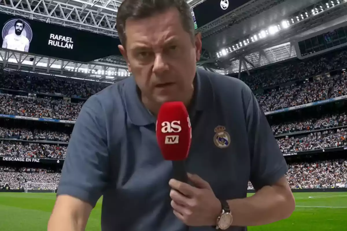 Un hombre con una camiseta del Real Madrid sostiene un micrófono rojo de AS TV en un estadio lleno de espectadores, con una pantalla en el fondo que muestra un homenaje a Rafael Rullán.