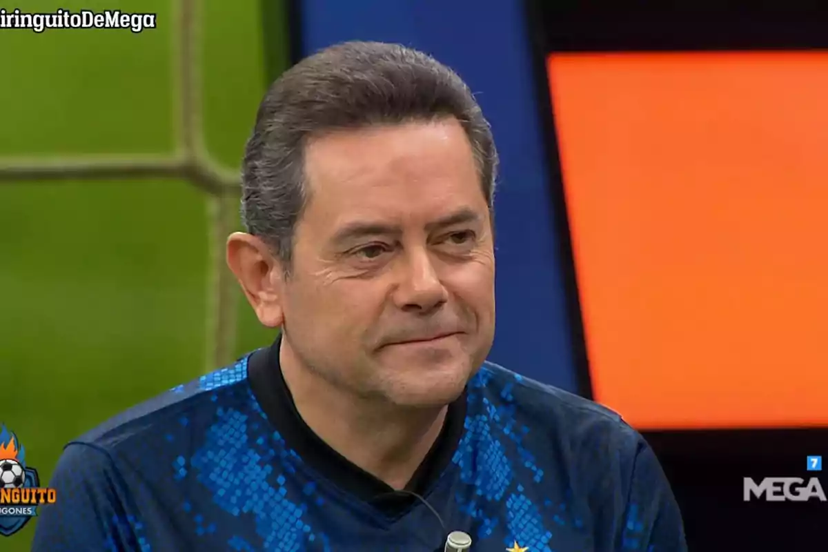 Un hombre con una camiseta azul sonríe mientras está en un programa de televisión.