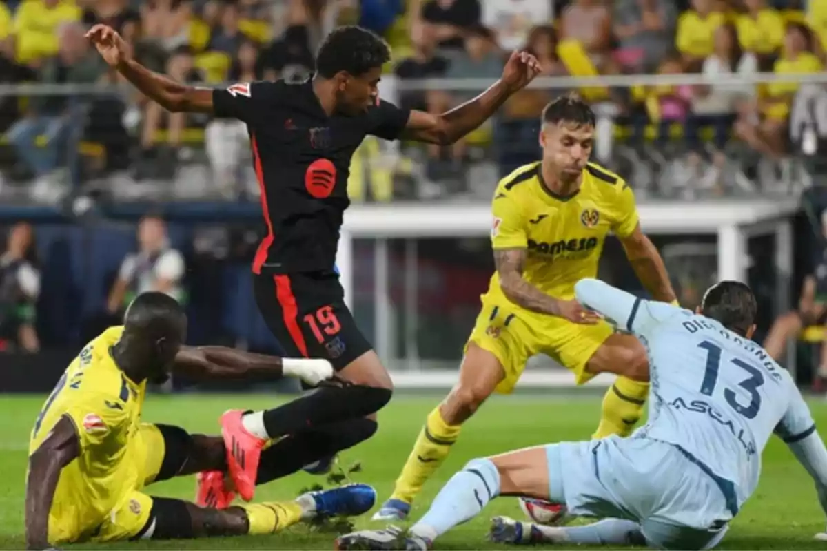 Soccer players in action during a match, one of them tries to dodge the defenders while the goalkeeper dives to the ground.