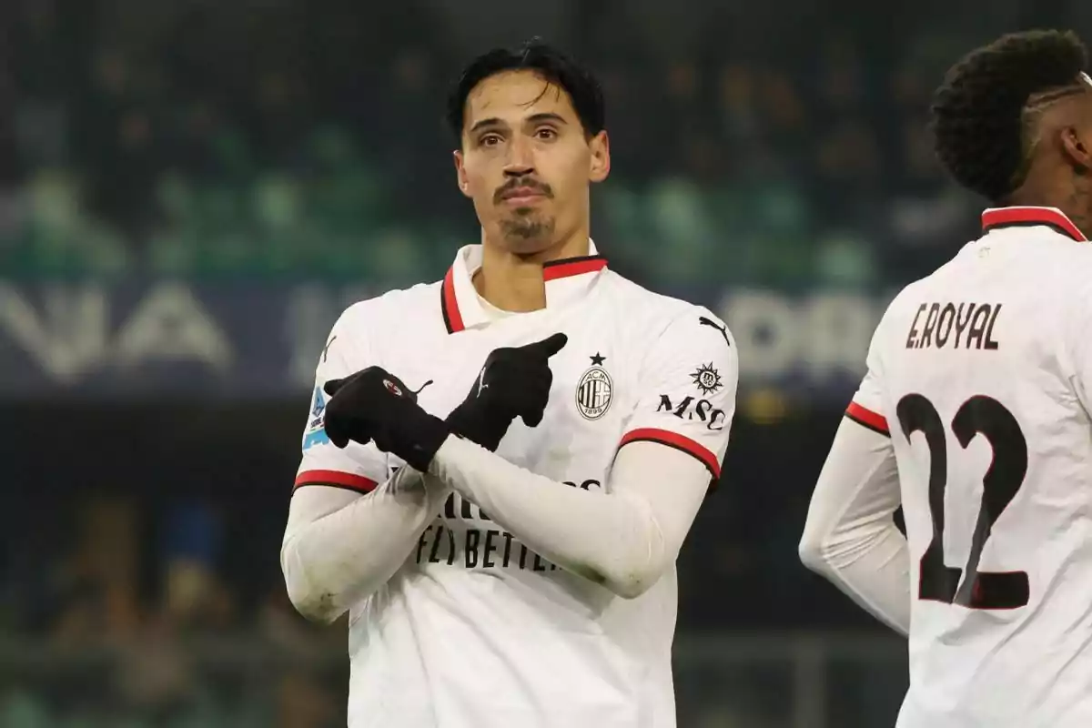 A soccer player in a white uniform gestures with his hands on the field while another player stands with his back turned. A soccer player in a white uniform gestures with his hands on the field while another player stands with his back turned.
