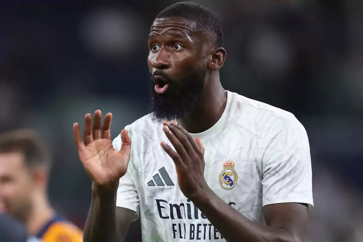 Un jugador de fútbol con camiseta blanca gesticula con las manos durante un partido.