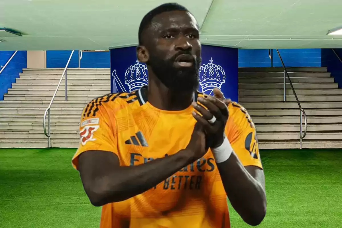 A player in an orange uniform applauds in a stadium with stairs and a shield in the background.