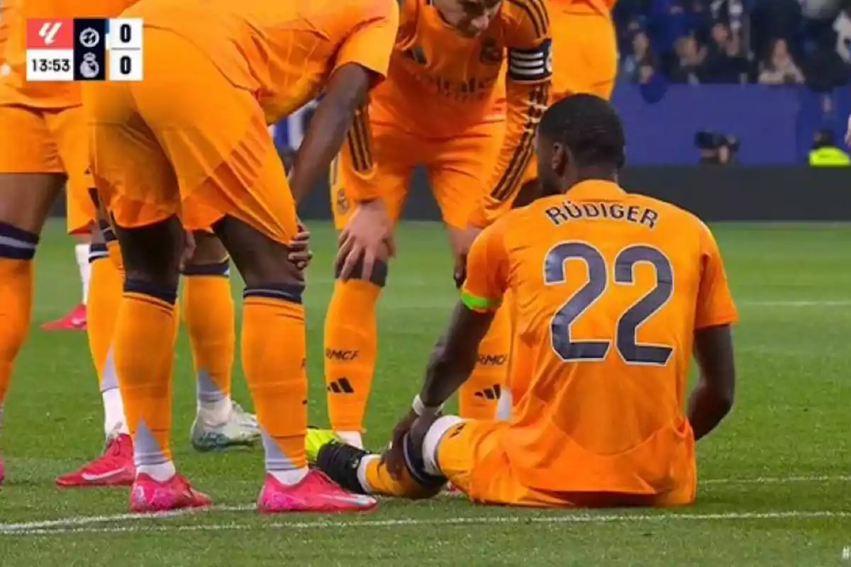 A player with the number 22 on his jersey is sitting on the field while his teammates surround him, all wearing orange uniforms.