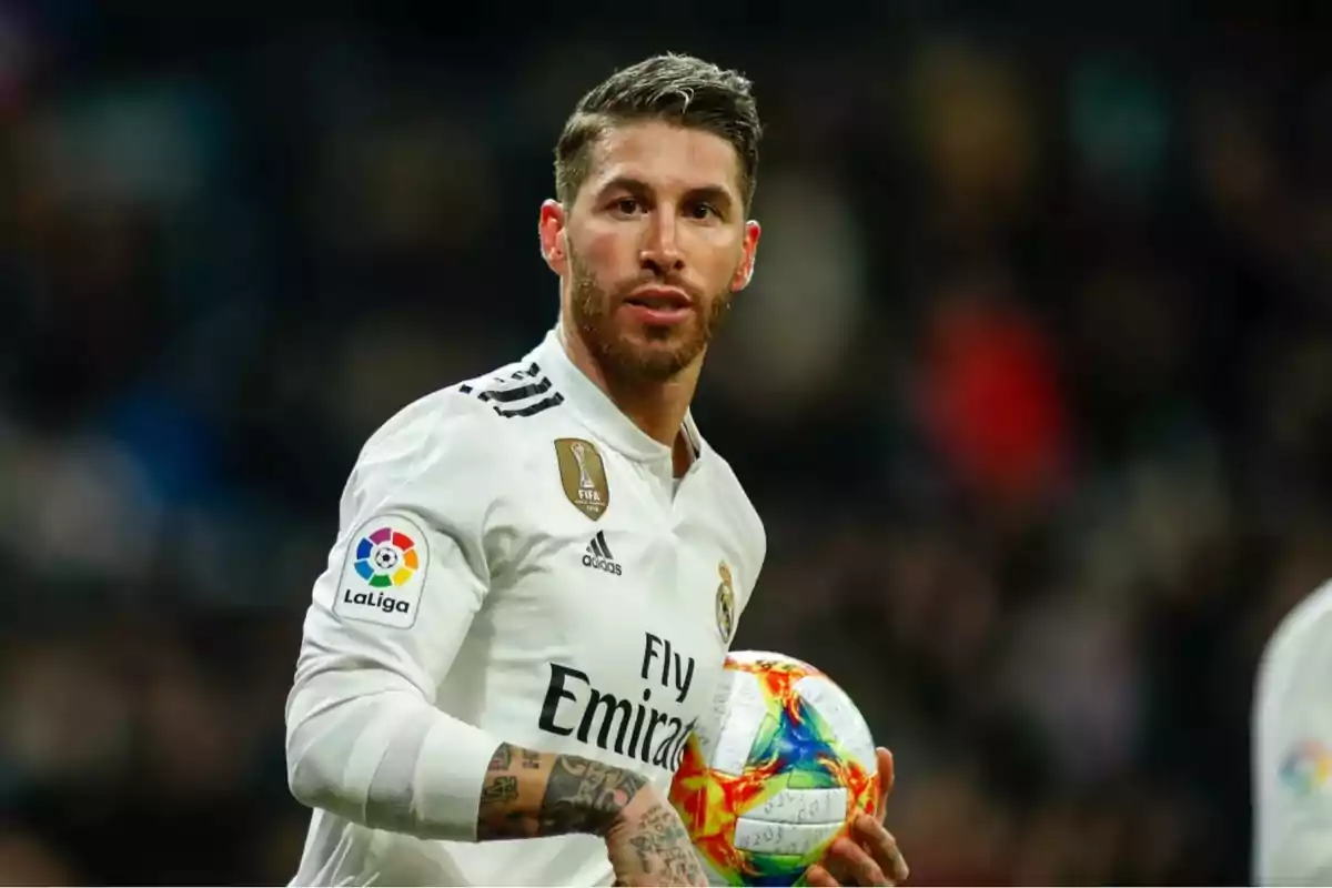 Un jugador de fútbol con uniforme blanco sosteniendo un balón en el campo.