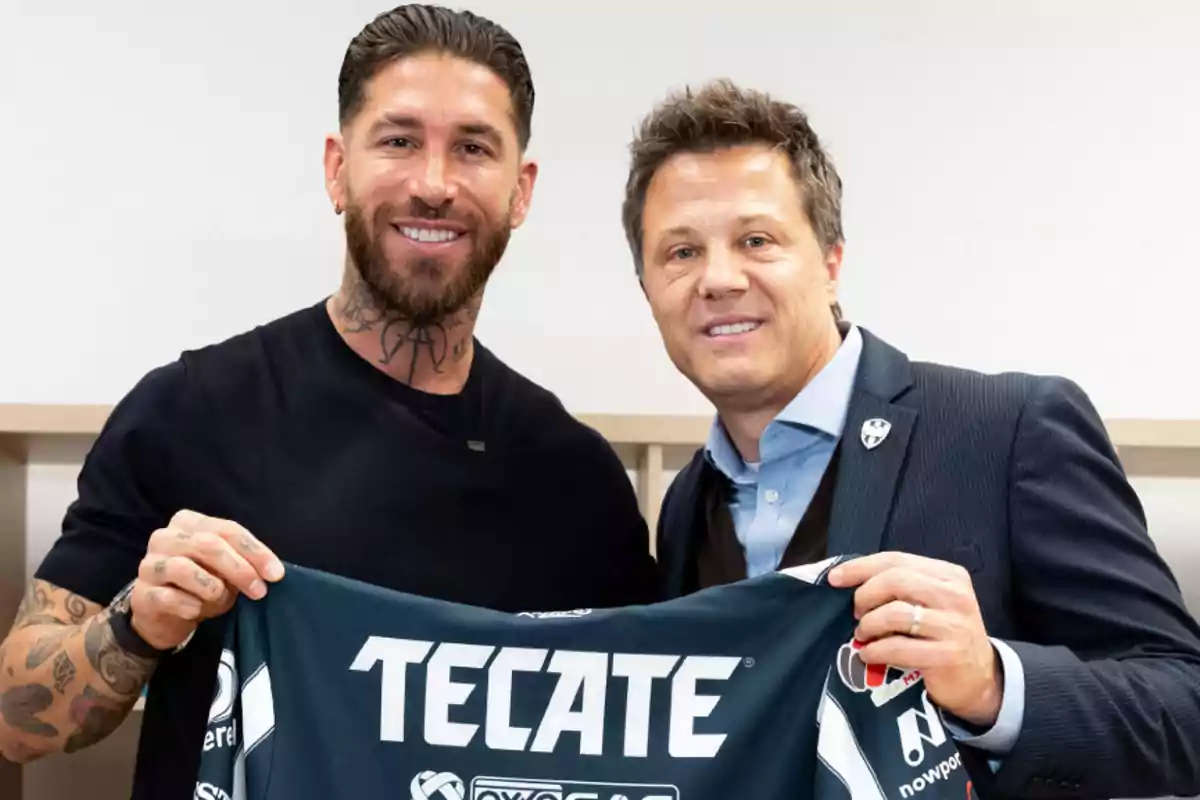 Dos personas sonrientes sostienen una camiseta de fútbol con el logo de una marca visible.