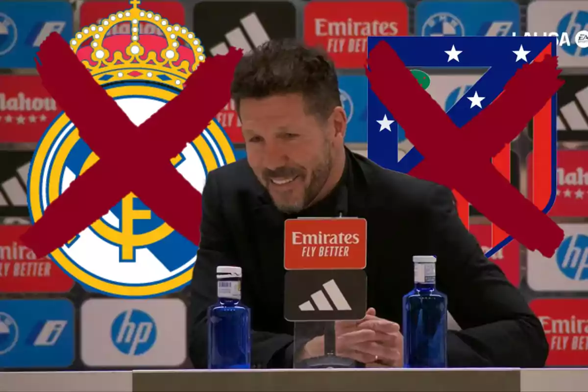 Un hombre sonríe en una conferencia de prensa con los logotipos del Real Madrid y Atlético de Madrid detrás, ambos tachados con una X roja.