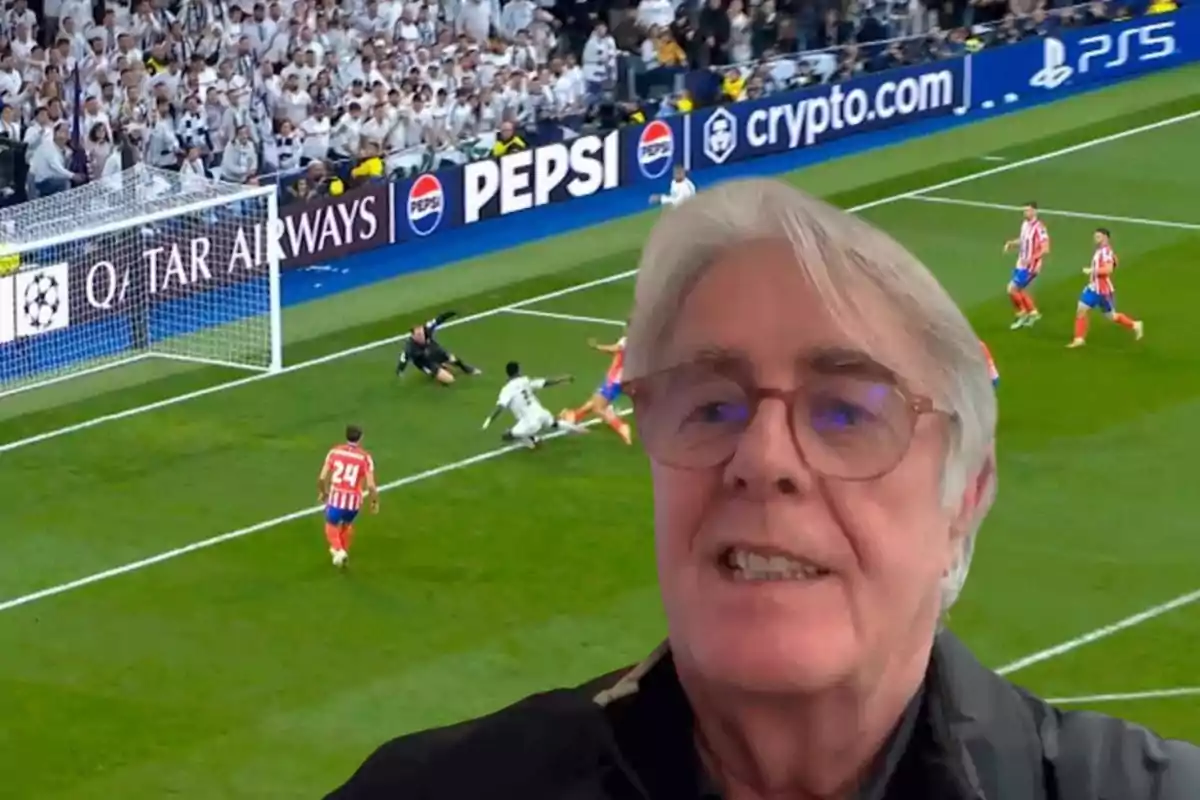 Un hombre con gafas aparece en primer plano mientras de fondo se observa una escena de un partido de fútbol con jugadores en acción cerca de la portería.