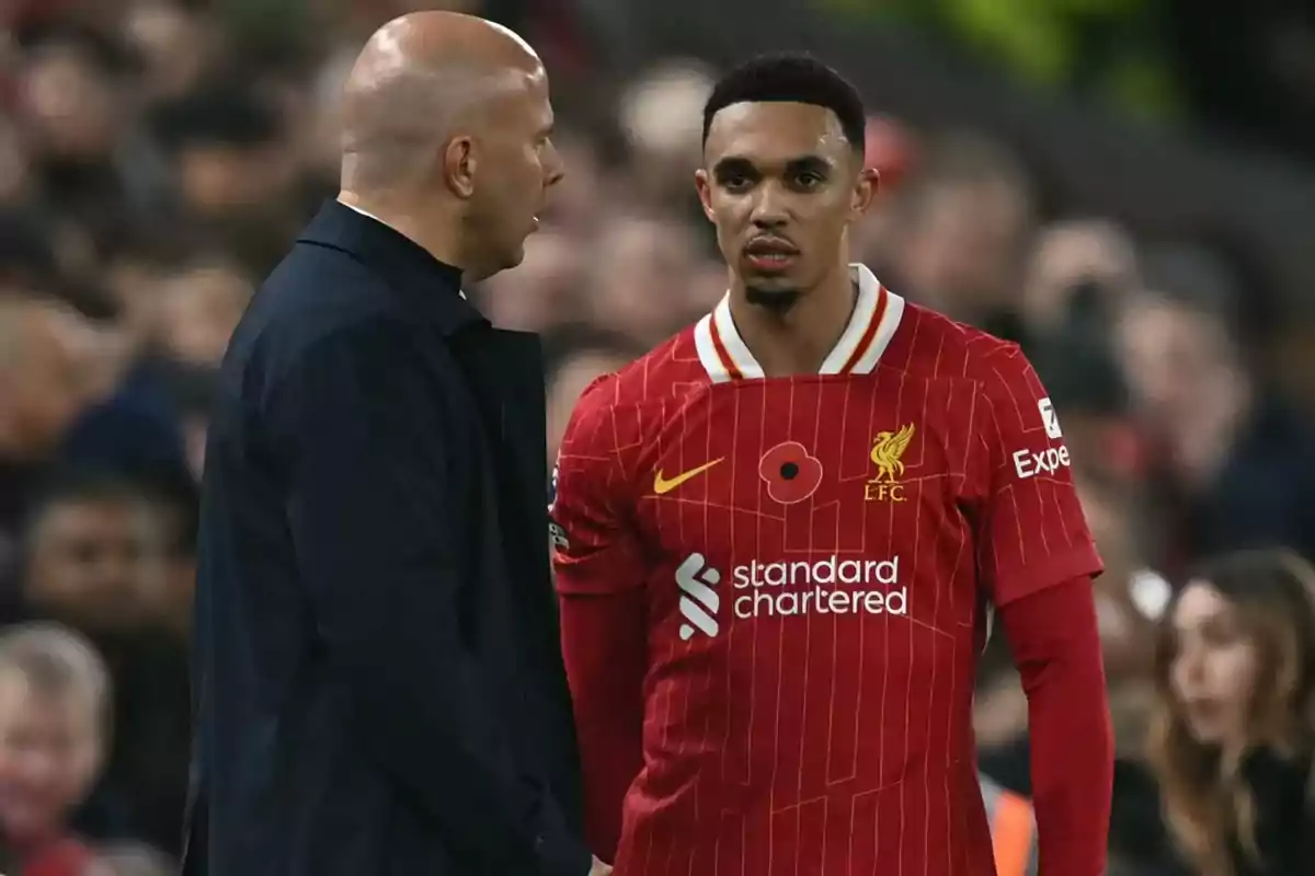 A player from Liverpool in a red uniform listens to a bald man who seems to be giving him instructions during a match. A player from Liverpool in a red uniform listens to a bald man who seems to be giving him instructions during a match.